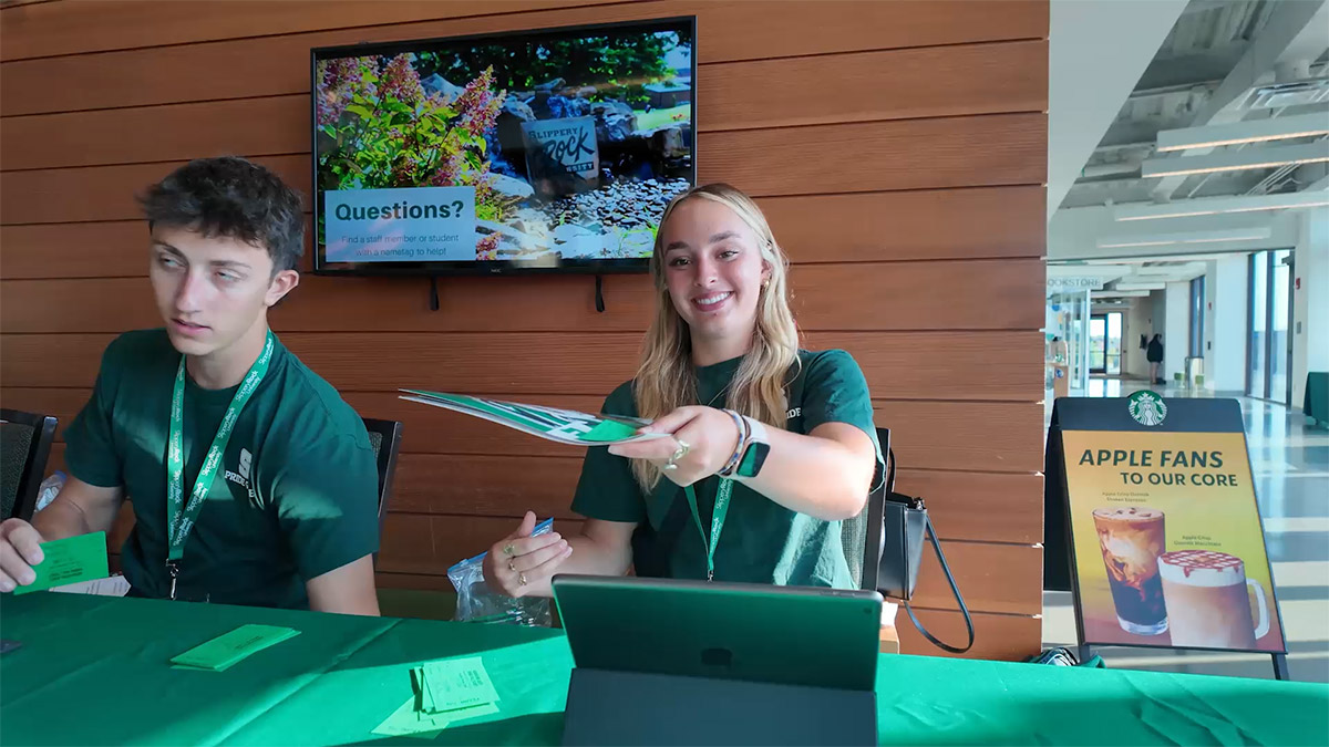 Two students smiling and handing out promotional materials.