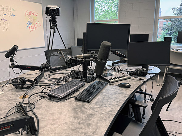 An image depicting a long and narrow desk with two microphone set ups sat across from each other.