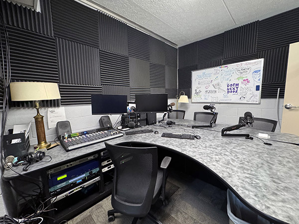 Image depicting a large desk with 3 microphone setups to be used during a radio broadcast.