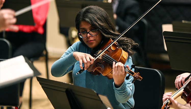 Music student playing violin with other students in the group